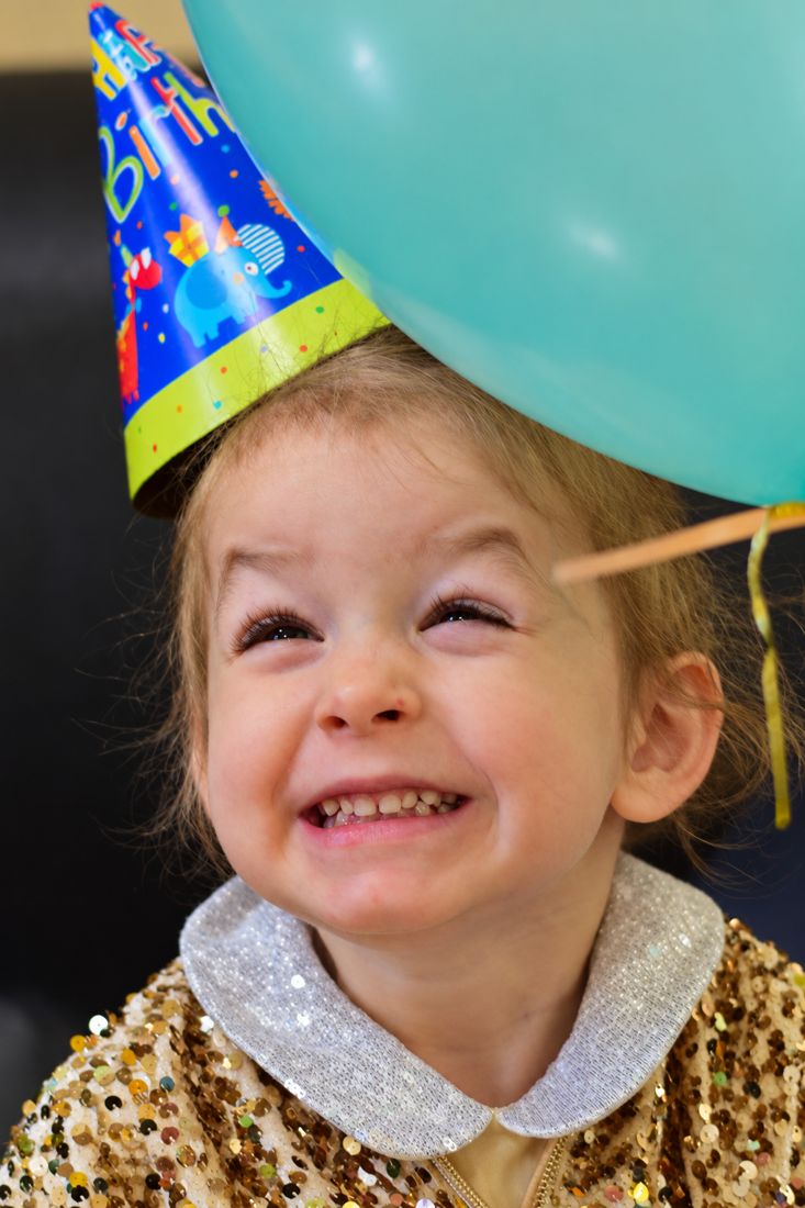 Mira con gorro de cumpleaños y un globo turquesa, riendo con los ojos cerrados